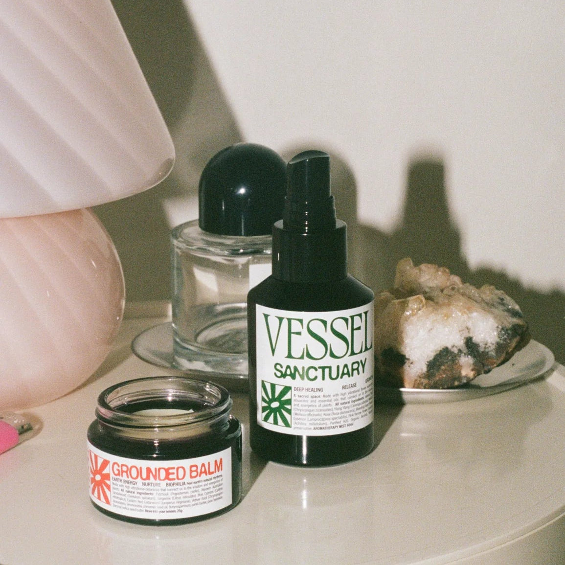 Two skincare products, a jar and a bottle labeled 'Vessel Sanctuary', on a white surface with a blurred background.